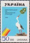 На фоне голубого неба белый аист, в клюве эмблема Европейского года охраны природы
