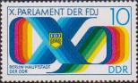Римская цифра «X», составленная цветной лентой, значок ССНМ и текст: «Берлин - столица ГДР»